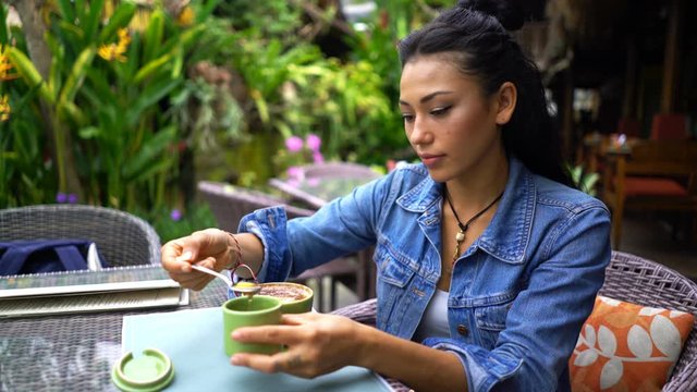 Woman add sweet honey and mixing coffee sitting at garden cafe