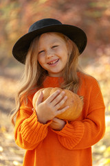 Little cute girl in the autumn forest with a ripe pumpkin in the hands. Autumn mood. Thanksgiving Holiday Concept.