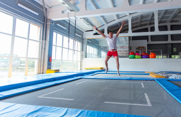 Fitness, fun, leisure and sport activity concept - Handsome happy man jumping on a trampoline indoors