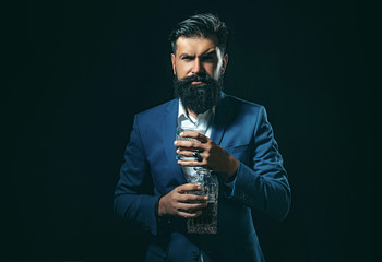 Naklejka premium Cheerful bearded man is drinking expensive whisky. Degustation of elite alcohol. Elegant and stylish man in classical wear holding glass with wiskey in hand.
