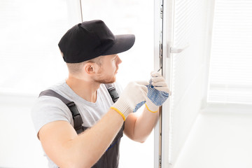 Construction worker man uses screwdriver to screw handle install plastic white upvc windows in house