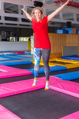 Fototapeta na wymiar Fitness, fun, leisure and sport activity concept - Young happy woman jumping on a trampoline indoors