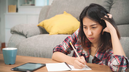 Asian student woman do homework at home, female using tablet for searching on sofa in living room at home. Lifestyle women relax at home concept.