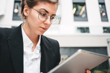 Close-up pensive young businesswoman sitting in cafe and using personal digital tablet for project social media. Creative female freelancer working in coffee shop