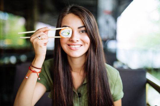 Young Woman Have A Sushi Holding Roll Under Her Eye In Cafe