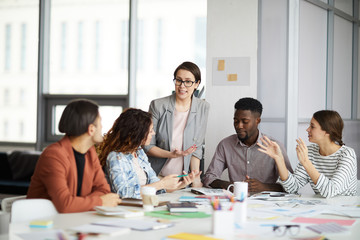 Diverse group of young business people discussing project sitting at table in modern office, focus on female manager giving instructions