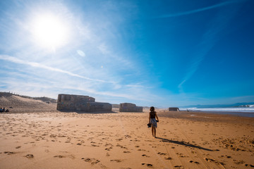 Labenne Océan, les Landes / France »; October 26, 2019: A young girl walking along Labenne Océan beach between world war bunkers and the sun in the background