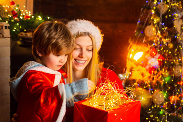 Fototapeta na wymiar Mother and son in Santa costume opening Christmas amazing gifts. Christmas eve. Holiday. Indoor. Home. Family winter holidays and people concept.