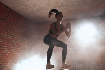Beautiful sporty woman in sportswear jumping on box in gym. Training, cross fit, sport. Brickwall...