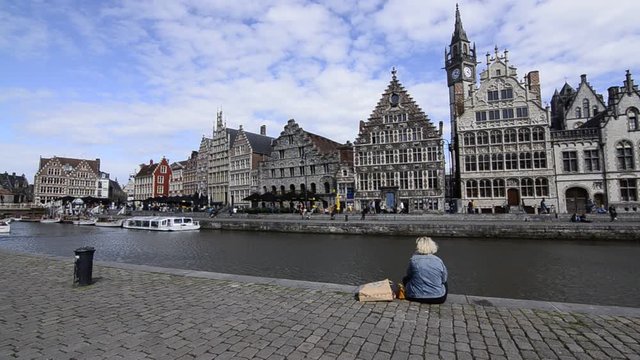 Ghent,Flanders,Belgium. August 2019. The fascinating historic center seen from the San Michele bridge. Canal view with beautiful buildings overlooking the water. A woman sitting on the shore. Tourists