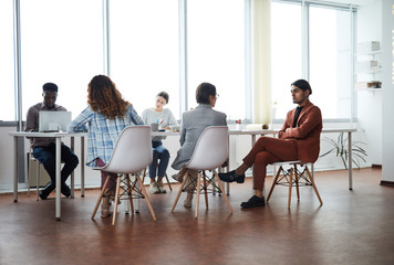 Obraz premium Wide angle view at contemporary business team working in modern office, focus on Middle-eastern young man sitting on chair, copy space