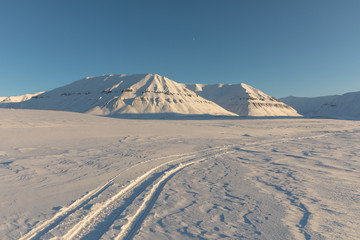 Fototapeta na wymiar Snowmobile tracks in arctic winter landscape with snow covered mountains on Svalbard, Norway