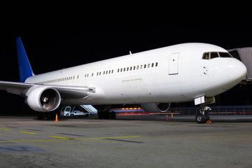 Big modern white aircraft on the parking area in the airport at night, front view