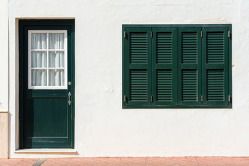 Fototapeta premium Traditional Spanish architecture with white facade and green doors and windows. Menorca, Spain