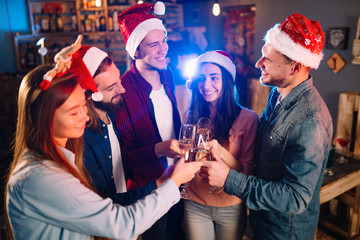 Friends celebrating new year's together. Portrait of Friends With Drinks Enjoying Cocktail Party. Young people laugh. Group of beautiful young people in Santa hats. Blur Background.