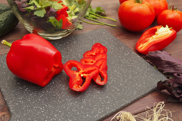 Sliced bellpepper on cutting board for salad among vegetables and greens on a wooden table
