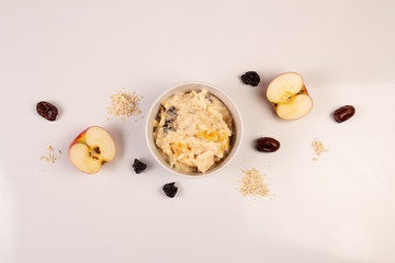 Salad of apple, orange, oat hops and prunes with honey in a white plate on a white background. 