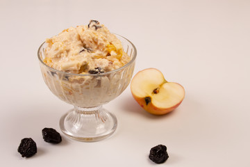 Salad of apple, orange, oat hops and prunes with honey in a glass plate on a white background. 