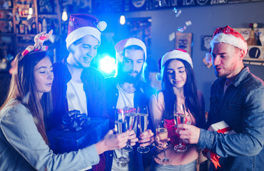 Friends celebrating new year's together. Portrait of Friends With Drinks Enjoying Cocktail Party. Young people laugh. Group of beautiful young people in Santa hats. Blur Background.