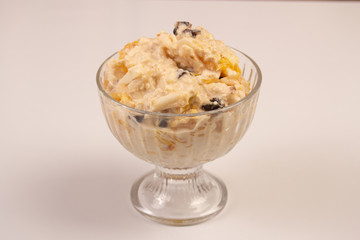 Salad of apple, orange, oat hops and prunes with honey in a glass plate on a white background. 