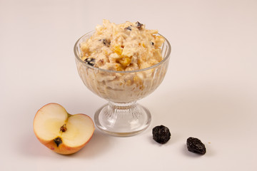 Salad of apple, orange, oat hops and prunes with honey in a glass plate on a white background. 