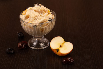 Salad of apple, orange, oat hops and prunes with honey in a glass plate on a brown background. 