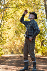 Bearded caucasian hunter wearing cowboy hat in search of trophy in autumn forest, look uo for wild bird. Stand looking for prey in hunting period, autumn season open.