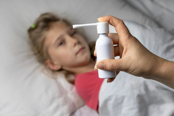 a girl with white hair lies in bed she is out of focus. mom using an inhaler makes an injection in the patient's throat, she is in focus.