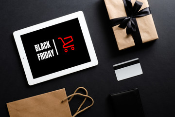 Black Friday sale concept. Tablet with sign "Black Friday" on screen, shopping bag and credit card over black background. Flat lay, top view, overhead.