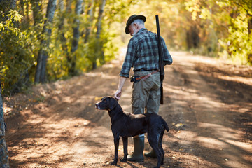 ambush for ducks with dog in autumn forest. Hunter man's back with dog going to hunt