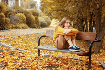 Monochrome autumn. Beautiful teenager girl in yellow hoodie and brown jeans sitting thoughtfully on...