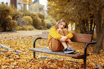 Monochrome autumn. Beautiful teenager girl in yellow hoodie and brown jeans sitting thoughtfully on...