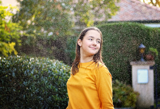 Happy smiling teenage girl enjoying rain and sun putting her face under water drops smiling happily. True happiness. Summer lifestyle.