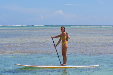 young woman practising paddle board or sup in tropical Caribbean sapphire crystal clear calm waters