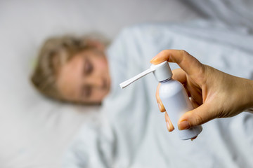 a girl with white hair lies in bed she is out of focus. mom using an inhaler makes an injection in the patient's throat, she is in focus.