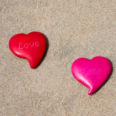 Two pink and red heart sitting on the sand at the beach