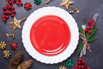 Christmas table place setting with empty red plate, cutlery with festive decorations snowflake star bow ball on stone background. Christmas and New Year holiday concept - Image
