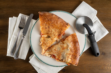 Layflat from above two slices from large double crust pizza with slicing tool and cutlery and white cotton napkins