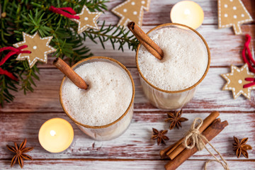Eggnog in glass cups with a delicate foam, spices and a cinnamon stick