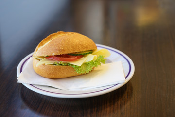 bread roll bun with cheese, tomato and lettuce served as breakfast or fast snack on a plate on a dark wooden table, copy space