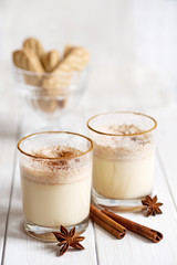 Eggnog in glass cups with a delicate foam, spices and a cinnamon stick