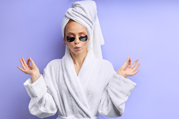 Keep calm after shower, wearing black patches under eyes. Girl in bathrobe and towel, isolated over purple background. Keep calm, skin care, careful