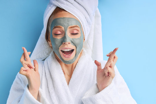 Woman with towel in bathrobe using mask. Excited with cosmetic procedures. Isolated over blue background