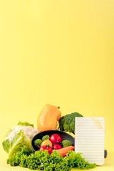 Vegetables and notebook with copy space on yellow background. Bio Healthy food, Organic vegetables on yellow background
