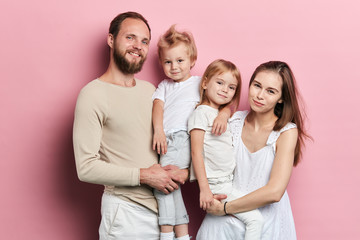 Obraz premium Happy young family with adoravle little daughters posing on pink background, close up portrait, solated pink background studio shot. relationship