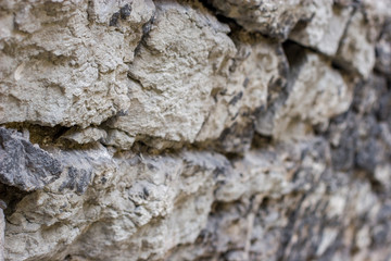 Texture background. Antique flagstone natural stone wall with selective shallow focus at the beginning and blurred distal part. Gray stones are laid with mortar.