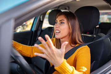 Plakat Beautiful angry woman honking in her car while driving. Angry woman driving a car. The girl with an expression of displeasure is actively gesticulating behind the wheel of the car.