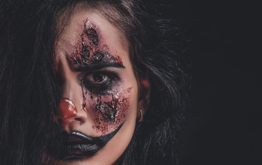 Closeup photo shoot of spooky girl with evil clown makeup at dark photo studio.