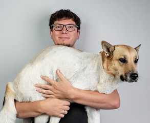 Funny caucasian man folding his mixed breed dog over grey background