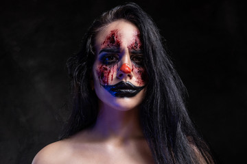 Portrait of spooky evil joker with scary makeup at dark photo studio.